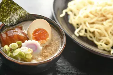 Close up shot of a bowl of noodles and a bowl of ramen soup with a poached egg, sliced in half.