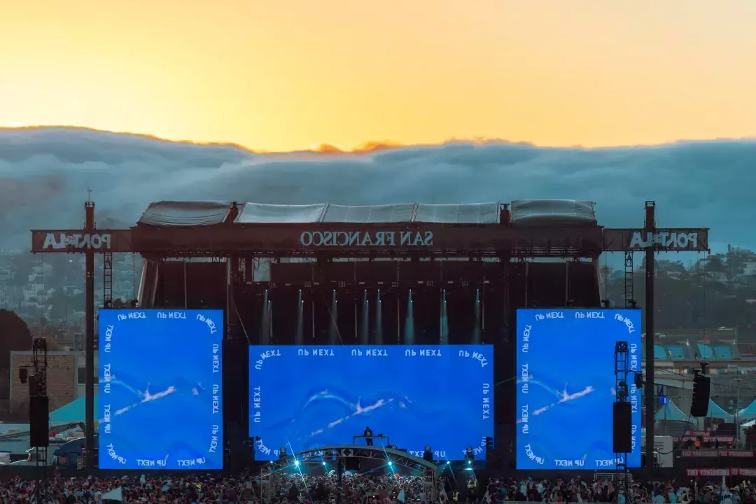 Fog spilling down San Francisco hills behind stage for music festival at sunset.